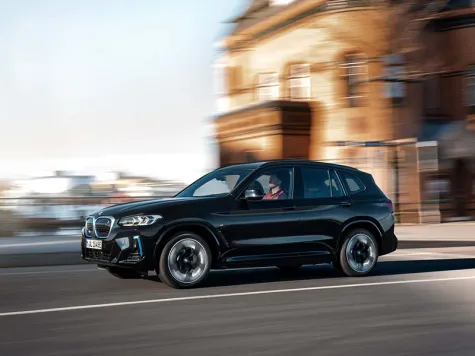 BMW iX3 Elektroauto in der Farbe Blau Ansicht von schräg vorne während einer Stadtfahrt BMW iX3 Elektroauto in der Farbe Blau Ansicht von schräg vorne während einer Stadtfahrt