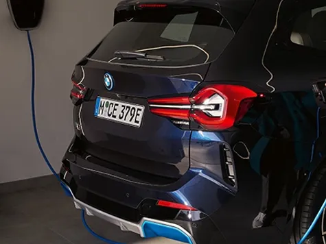 BMW iX3 Elektroauto in der Farbe Blau Ansicht von hinten beim Laden an einer Wallbox BMW iX3 Elektroauto in der Farbe Blau Ansicht von hinten beim Laden an einer Wallbox
