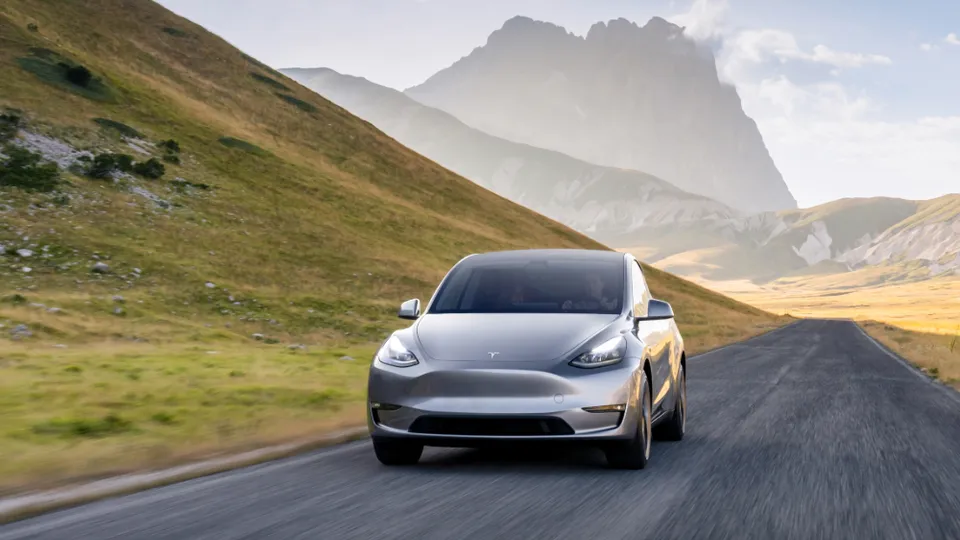 Tesla Model Y fährt auf einer Straße in einer leicht bergigen Landschaft. Tesla Model Y fährt auf einer Straße in einer leicht bergigen Landschaft.