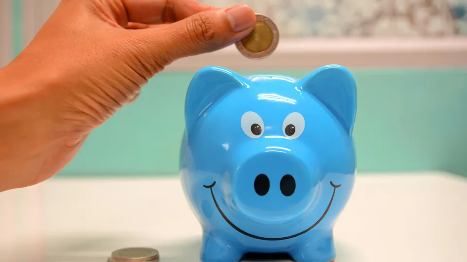 Hand schmeißt Geld in ein lachendes blaues Sparschwein Hand schmeißt Geld in ein lachendes blaues Sparschwein