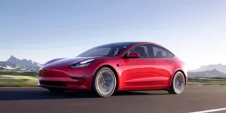 Tesla Model 3 Allrad in Rot fährt auf Strasse vor Bergen