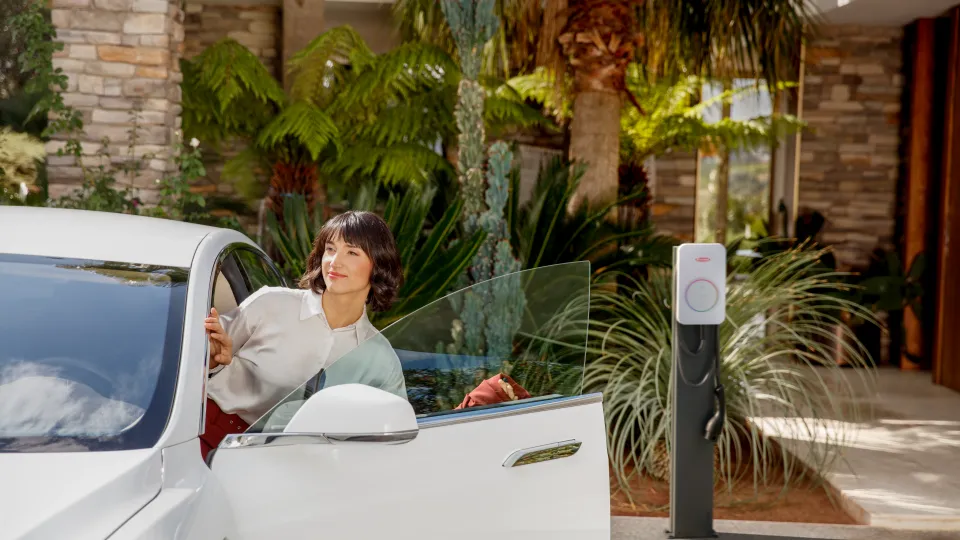 Frau steigt in ihr E-Auto mit AFIR-fähigem Fronius Wattpilot Flex Home im Hintegrund