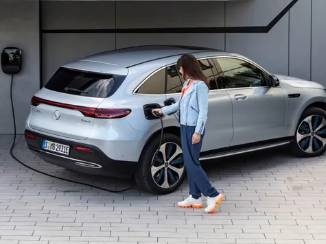 Mercedes EQC Elektroauto in der Farbe Silber Ansicht beim Laden an einer Wallbox. Frau mit Ladekabel