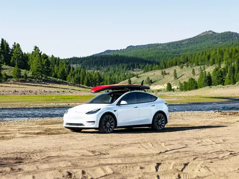 Tesla Model Y in Farbe weiß mit Surfbrett auf dem Dach Tesla Model Y in Farbe weiß mit Surfbrett auf dem Dach